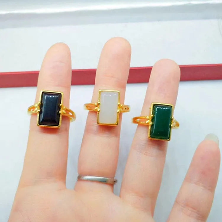 Adjustable brass gold-plated ring with a central green gemstone on a model's hand.