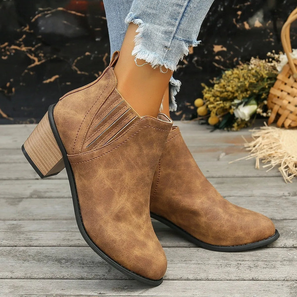 Black pointed toe ankle boots with a thick square low heel on a woman's foot.