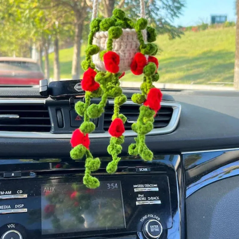 Green and white knitted wool car plant decoration with hanging rope on a car dashboard
