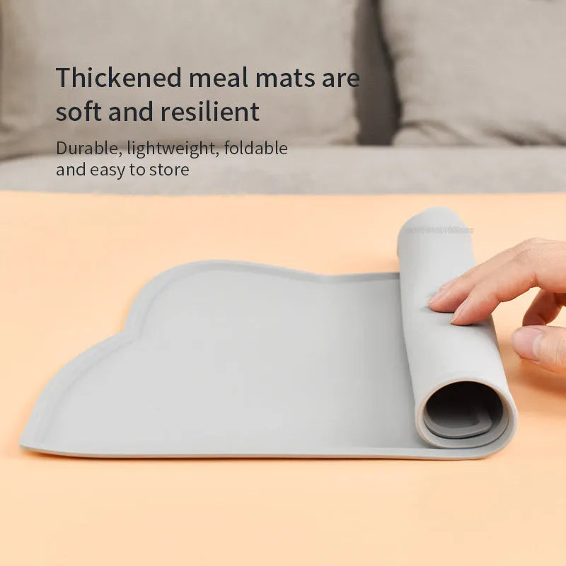 Solid colour silicone pet feeding mat in a cat head shape on a floor next to pet bowls.