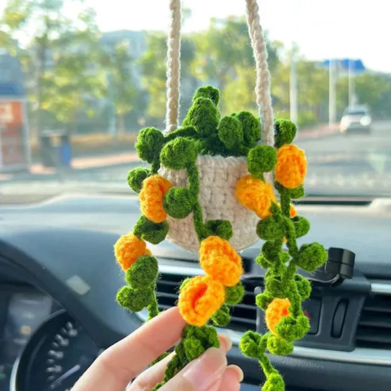 Green and white knitted wool car plant decoration with hanging rope on a car dashboard