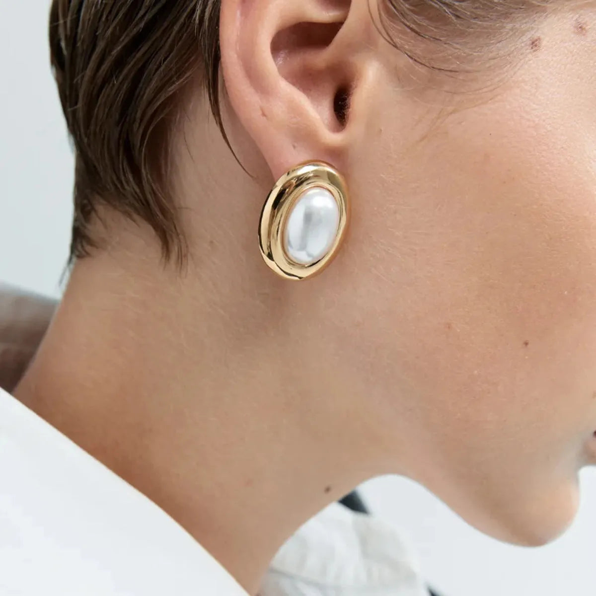 Small gold-tone stainless steel stud earrings with a white pearl accent on a grey background.