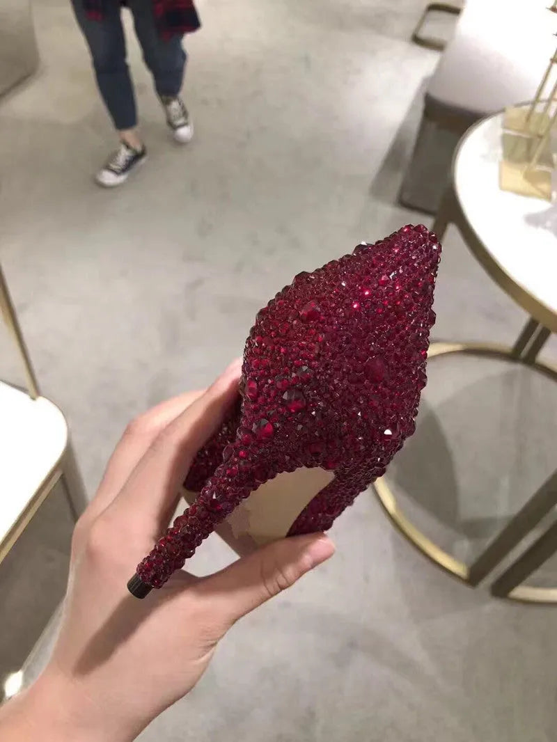 Gold women's pointed toe stiletto heels with rhinestone and bow decoration on a sequin cloth upper.