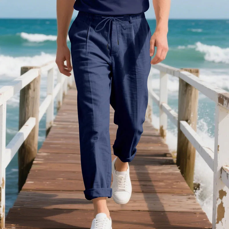 Men's straight leg linen trousers in light khaki colour with drawstring waist, laid flat.