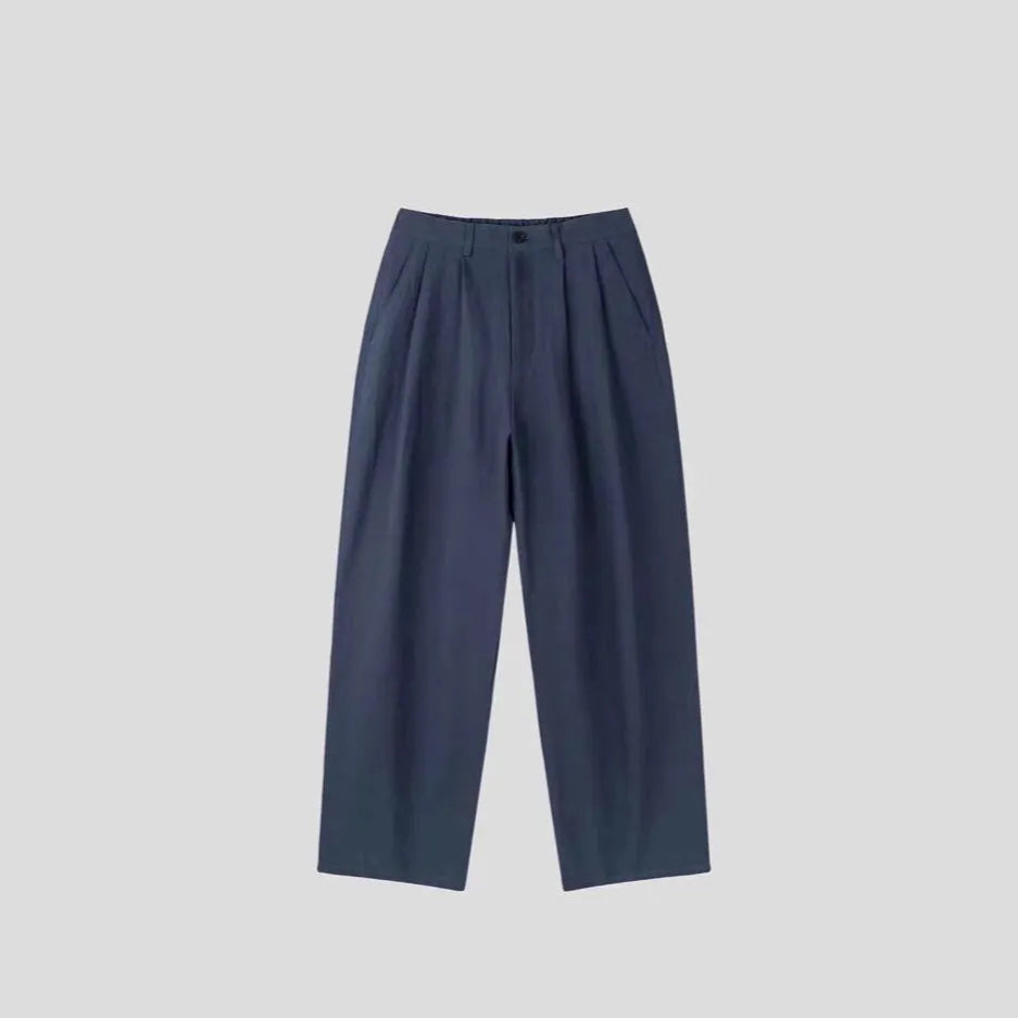 Man wearing apricot coloured loose wide-leg cotton linen trousers with a pencil leg opening.