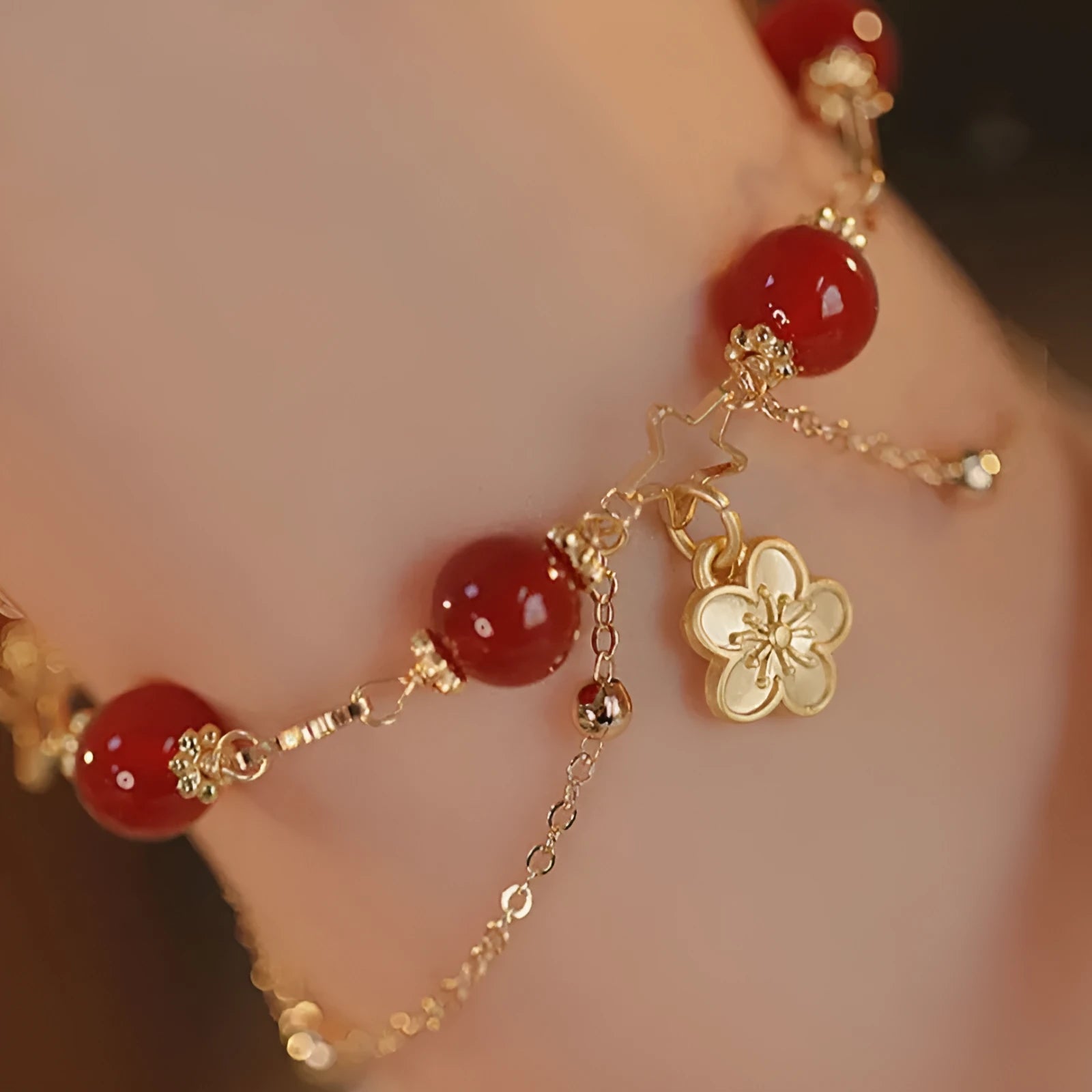 Red agate double layer bracelet with floral and peach blossom charms on a wrist.