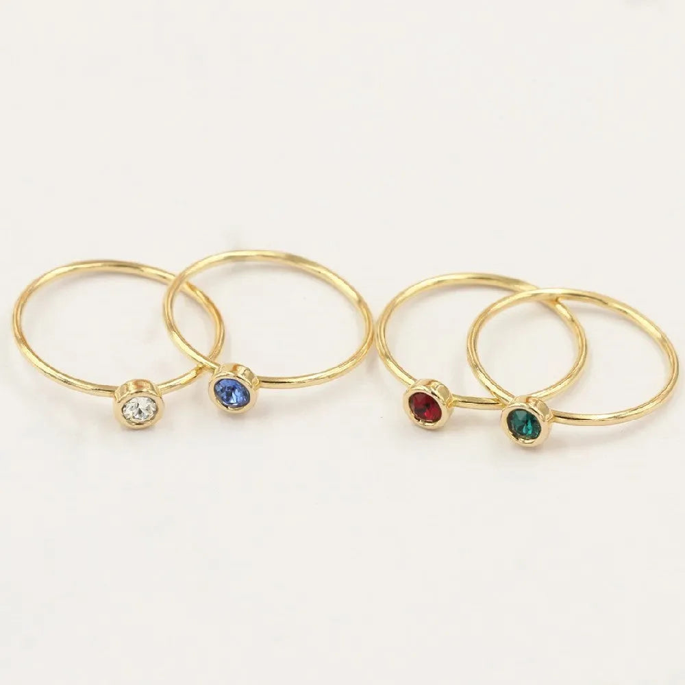 Women's 14K gilded gold-filled zircon copper knuckle ring in green, blue, dark red, or white on a finger.