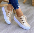 Women's white lace-up flat sneakers with silver rivet detailing on a round toe.