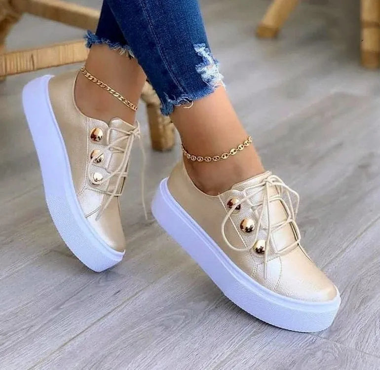 Women's white lace-up flat sneakers with silver rivet detailing on a round toe.