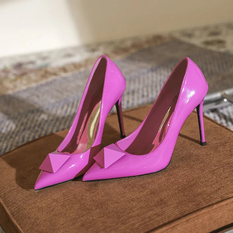 Women's pink patent leather pointed toe stiletto high heels with rivet and buckle decoration.