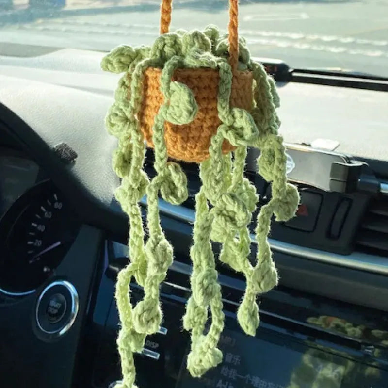 Green and white knitted wool car plant decoration with hanging rope on a car dashboard