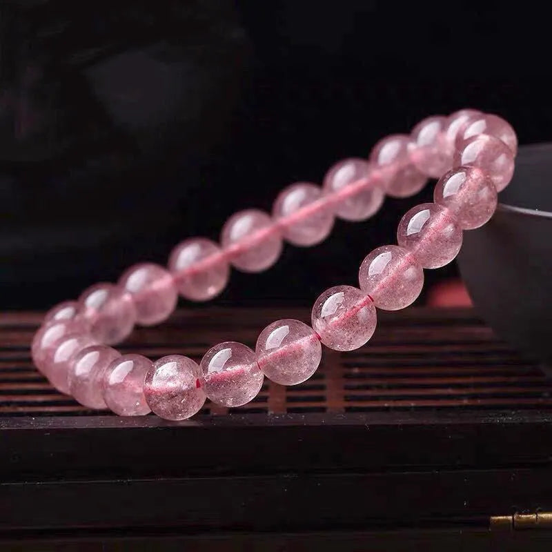 Women's strawberry quartz crystal bracelet with polished beads on a wrist.
