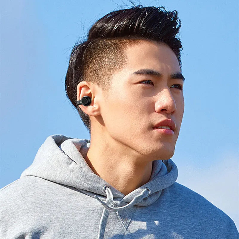 Black wireless Bluetooth clip-on earphones with bone conduction technology displayed beside charging cable