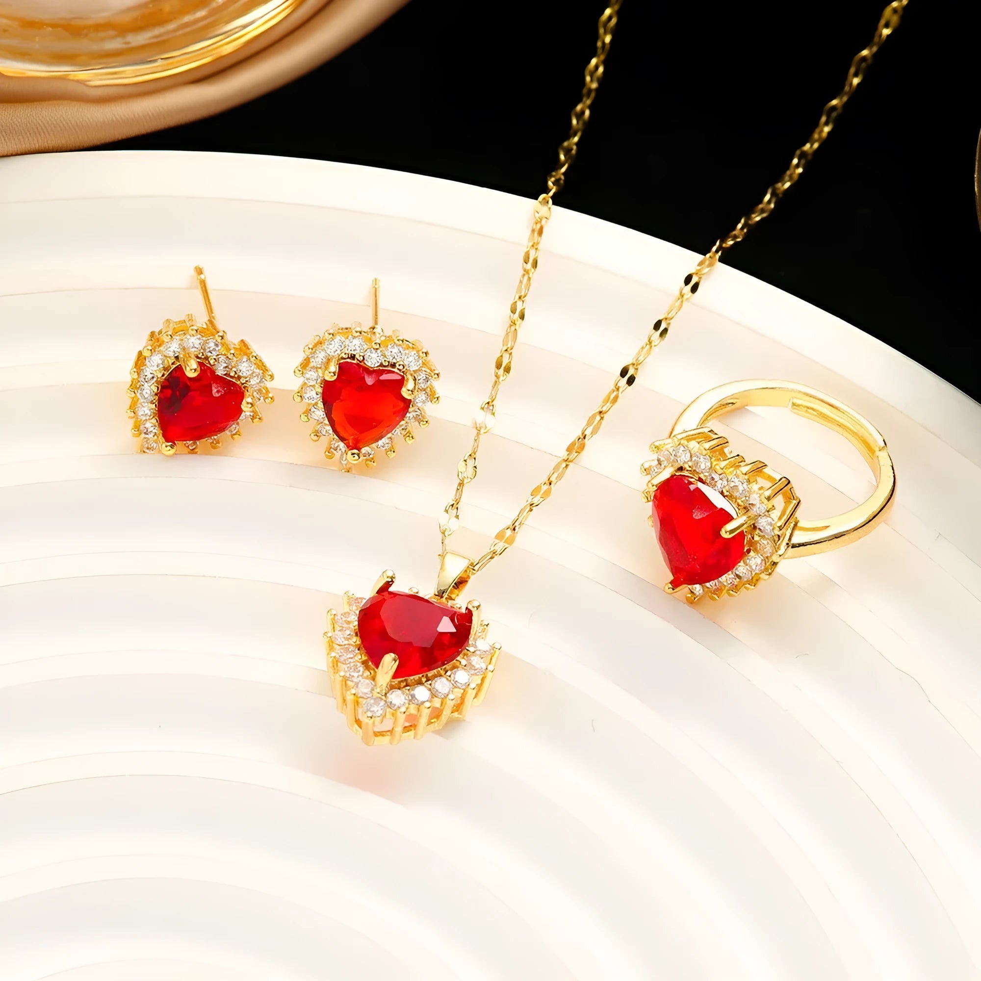 Women's heart-shaped jewellery set with matching necklace, stud earrings, and ring in electroplated gold red finish