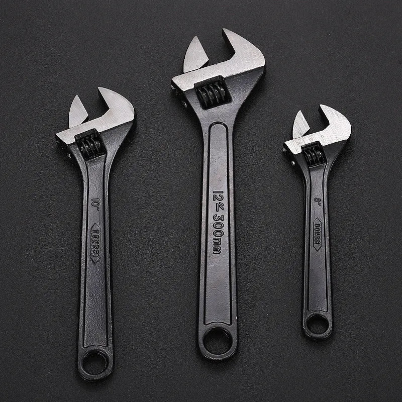 Black stainless steel adjustable open-end wrench on a workbench, showing size markings and ergonomic handle.