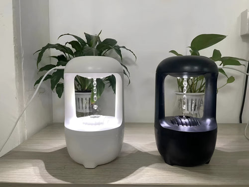White anti-gravity humidifier on a desk showing water droplets in mid-air backflow, with USB cable.