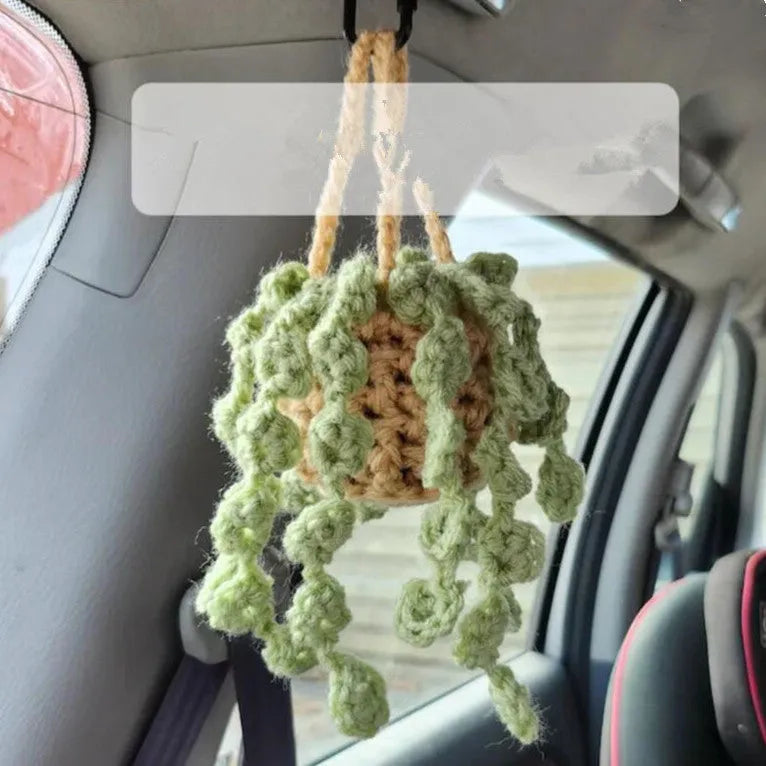Green and white knitted wool car plant decoration with hanging rope on a car dashboard