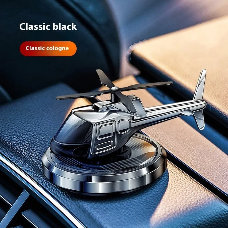 Silver metal solar helicopter car air freshener ornament with rotating blades on a car dashboard.