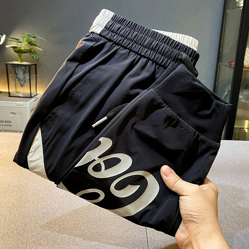 Black men's cropped casual trousers with an ankle-band cuff, laid flat to show the slim fit and cotton blend fabric.