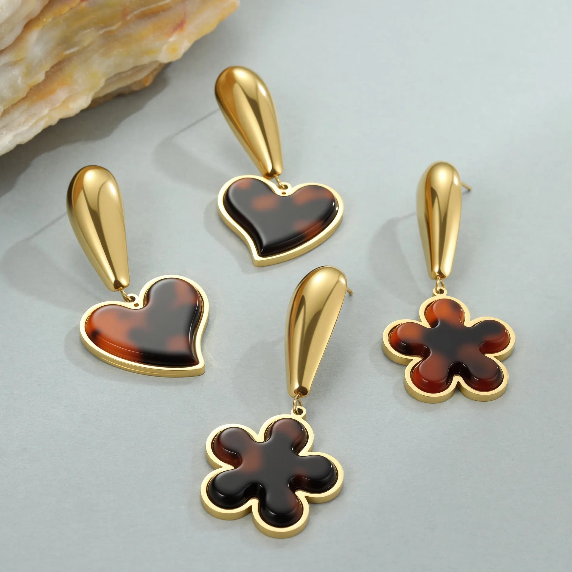 A pair of gold-coloured geometric earrings with a heart shape and a floral design on a white background.