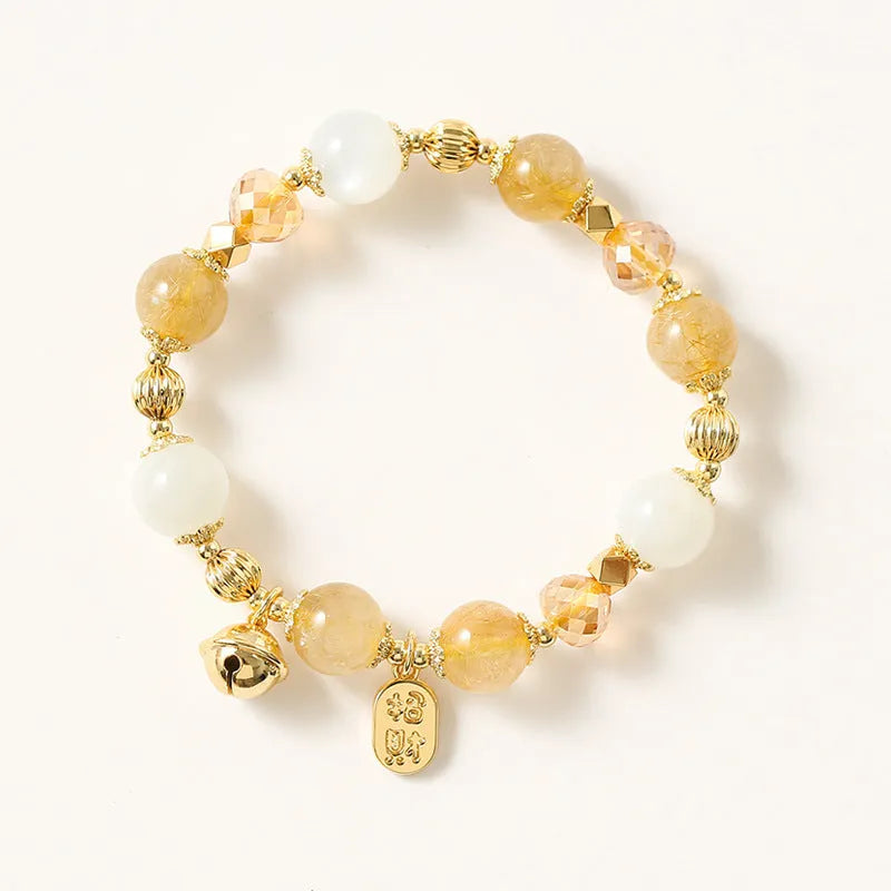 Gold rutilated quartz bracelet with bell charm on wrist