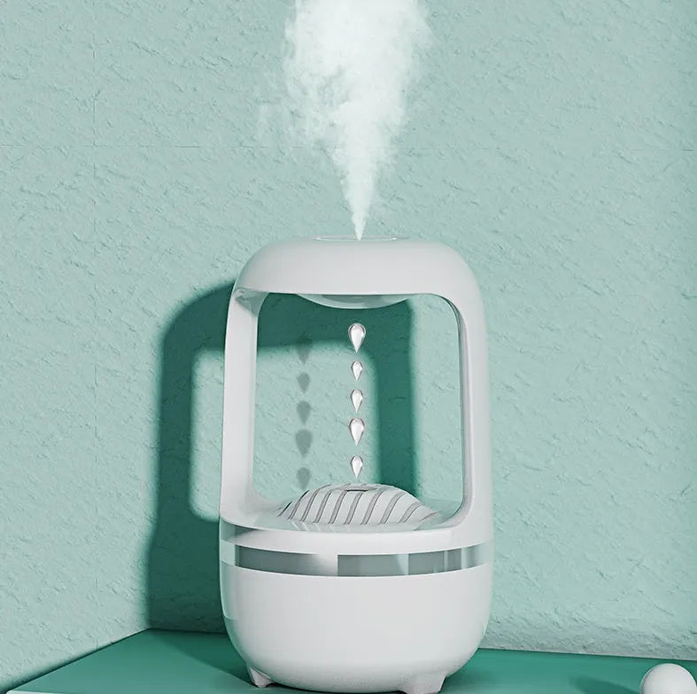 White anti-gravity humidifier on a desk showing water droplets in mid-air backflow, with USB cable.