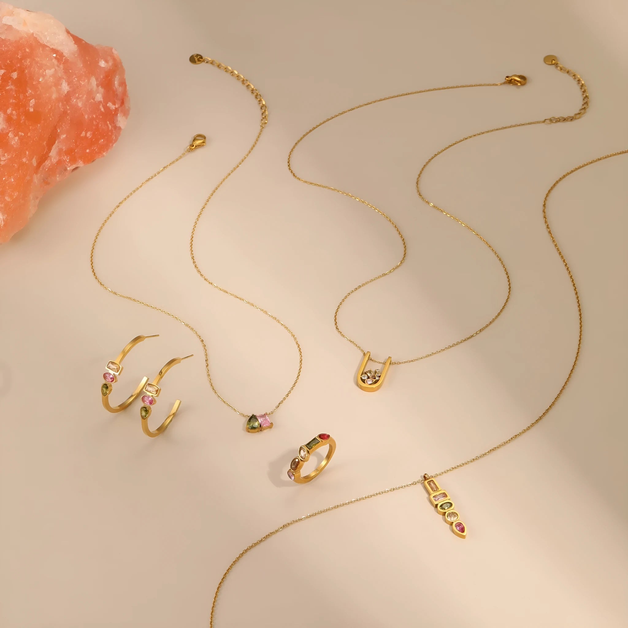 Geometric gold plated jewellery set with colour zircon necklace, ring, and earrings on a white background.