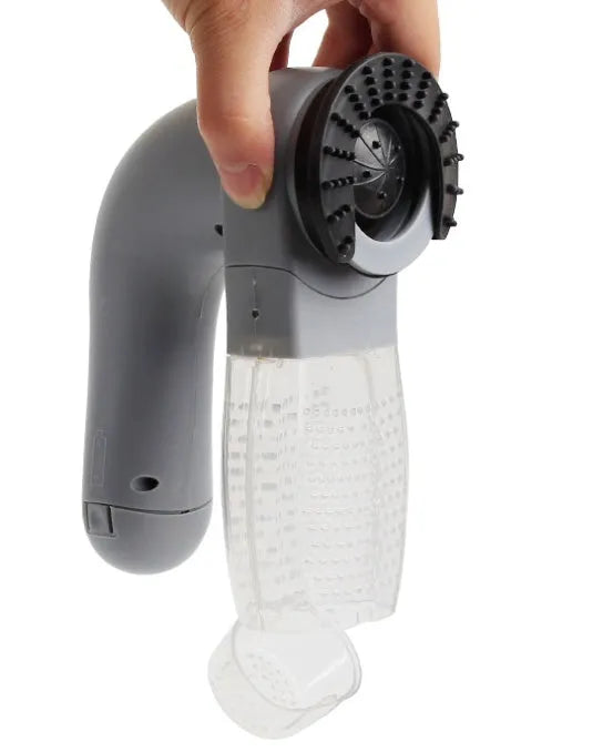 Grey handheld electric pet hair remover brush with soft rubber head, shown removing fur from upholstery.