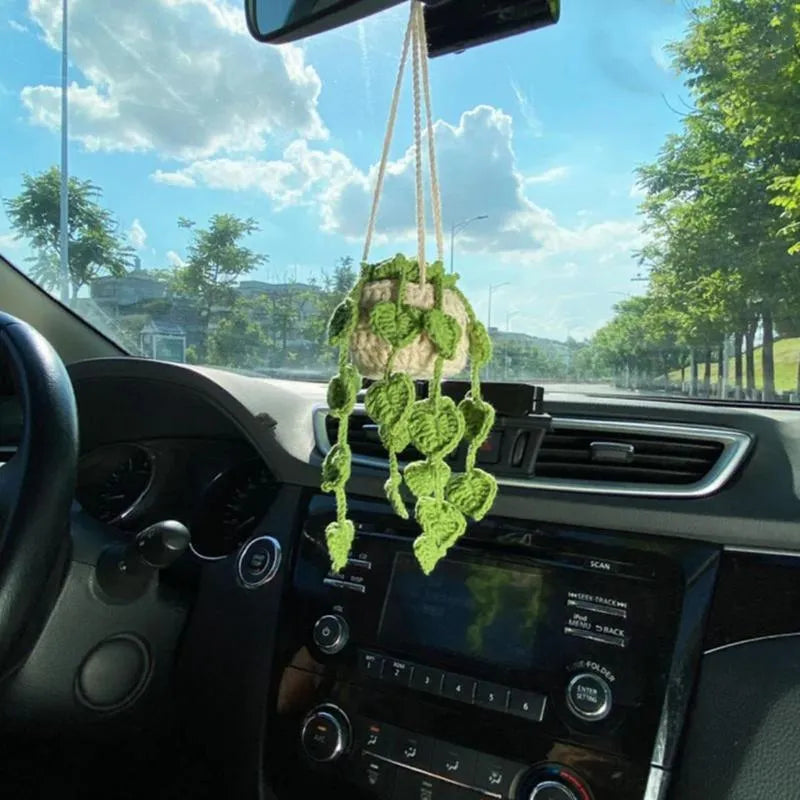 Green and white knitted wool car plant decoration with hanging rope on a car dashboard