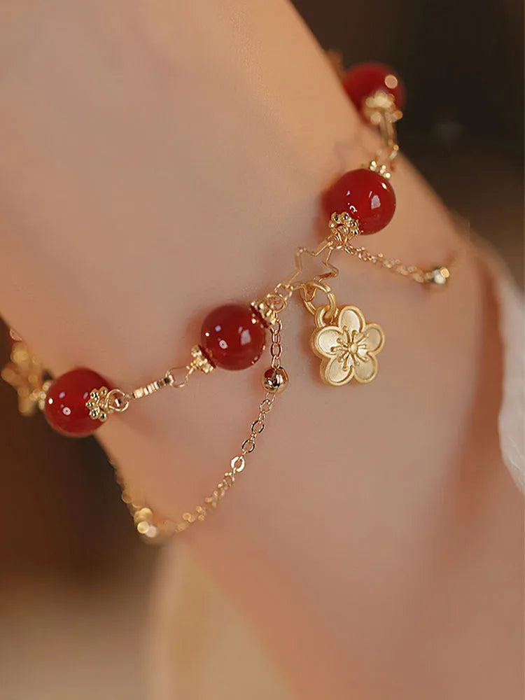 Red agate double layer bracelet with floral and peach blossom charms on a wrist.