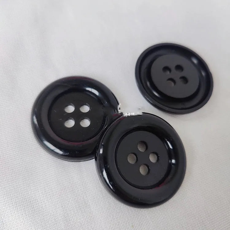 Plastic nylon oversized round button with four holes in various colours and sizes on a white background.