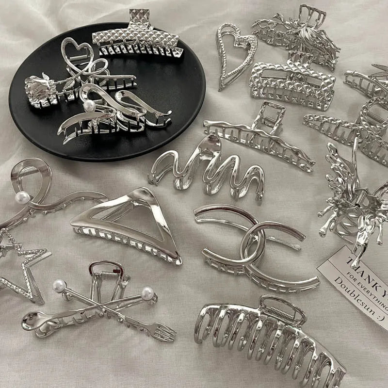Silver metal hair claw clip assortment showing bows, waves, pearl designs, and geometric shapes from 4cm to 13.5cm