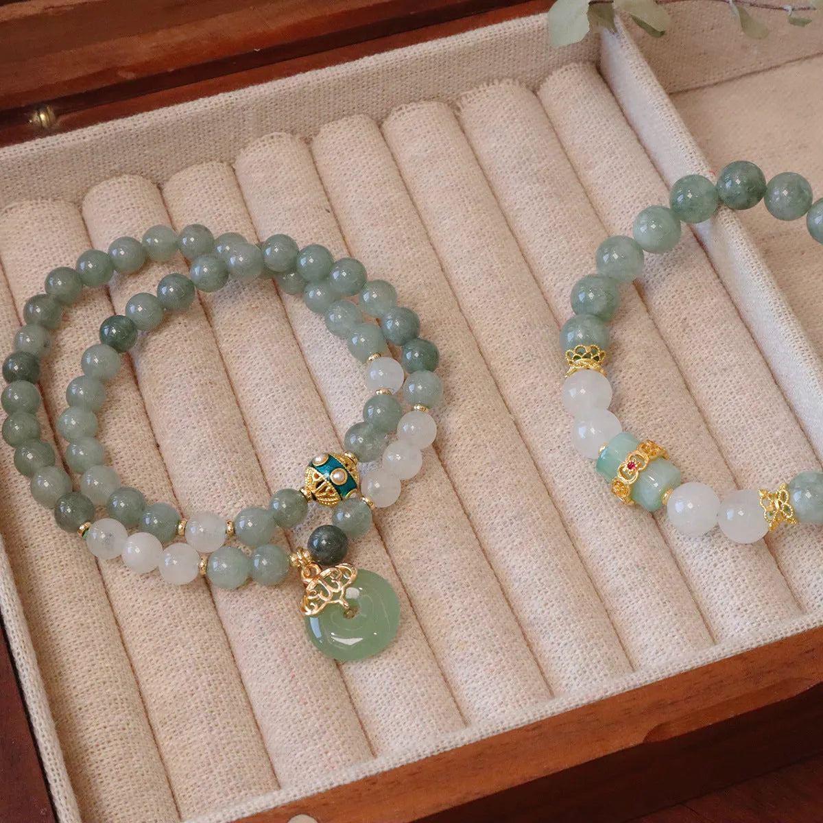 Close-up of a women's Myanmar jade bracelet with a silver geometric safety buckle pendant and lucky bead charms.