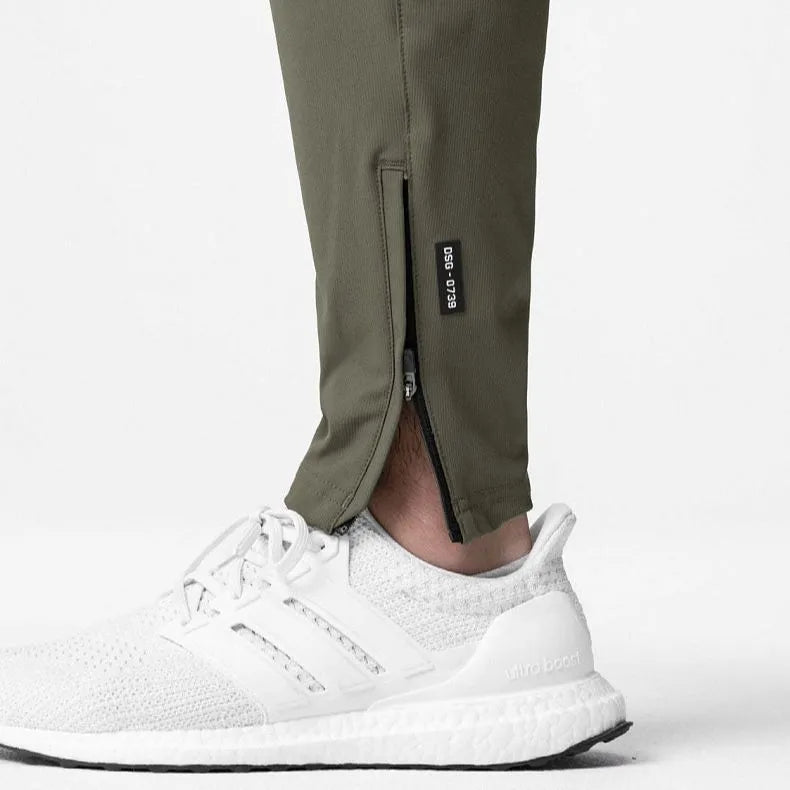 Men's loose grey fitness trousers with ankle ties on a gym floor.