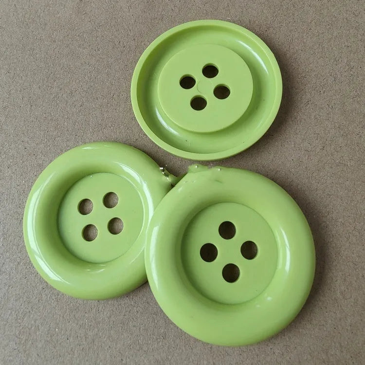 Plastic nylon oversized round button with four holes in various colours and sizes on a white background.