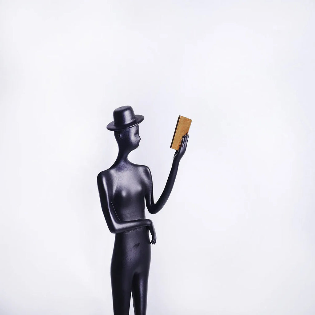 Black metal desktop sculpture of a woman reading, 51cm tall.