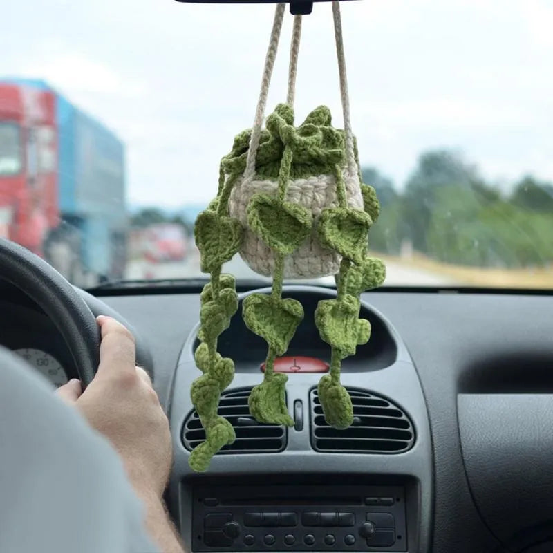 Green and white knitted wool car plant decoration with hanging rope on a car dashboard