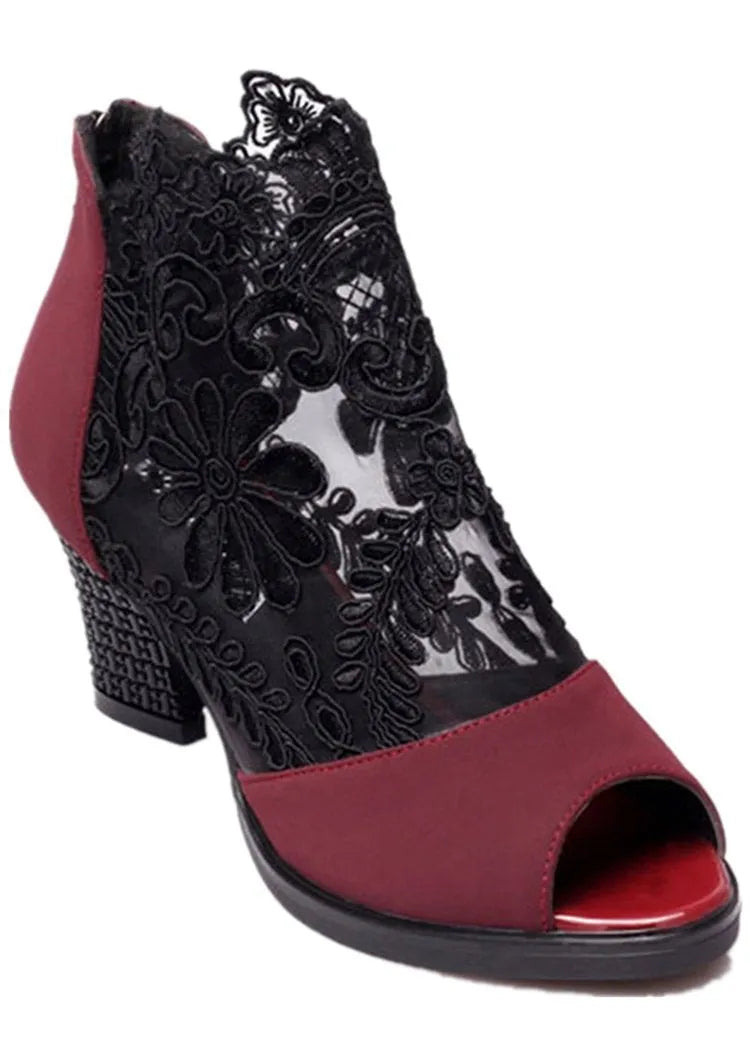 Black lace gladiator sandals with a flower motif, square high heel, and a front zip closure on a woman's foot.