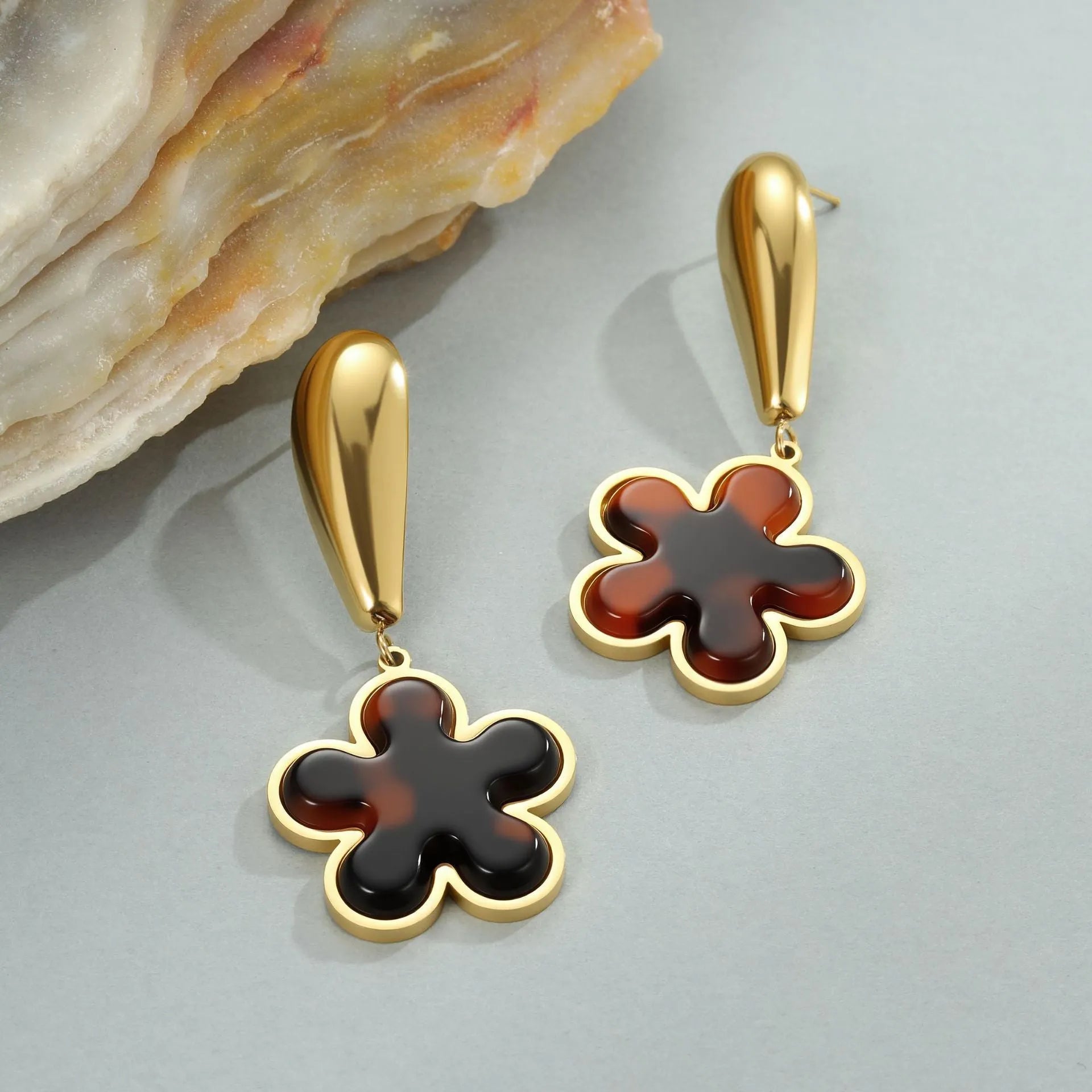 A pair of gold-coloured geometric earrings with a heart shape and a floral design on a white background.