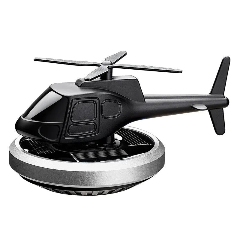Silver metal solar helicopter car air freshener ornament with rotating blades on a car dashboard.