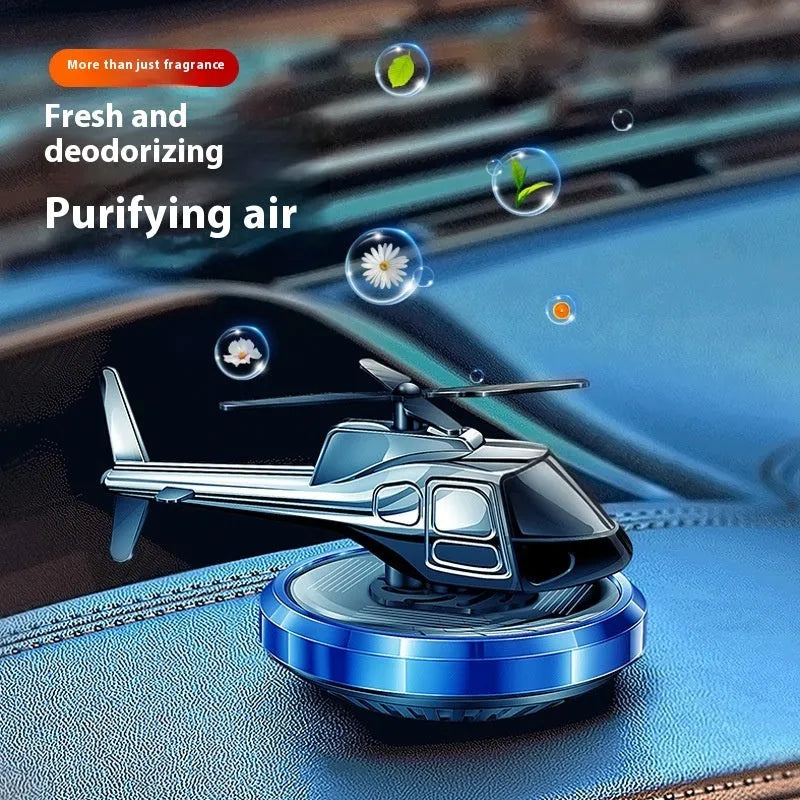 Silver metal solar helicopter car air freshener ornament with rotating blades on a car dashboard.