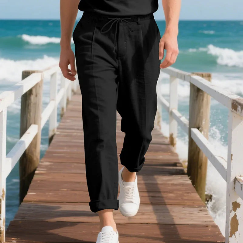 Men's straight leg linen trousers in light khaki colour with drawstring waist, laid flat.