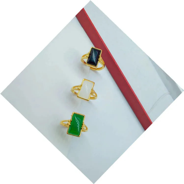Adjustable brass gold-plated ring with a central green gemstone on a model's hand.