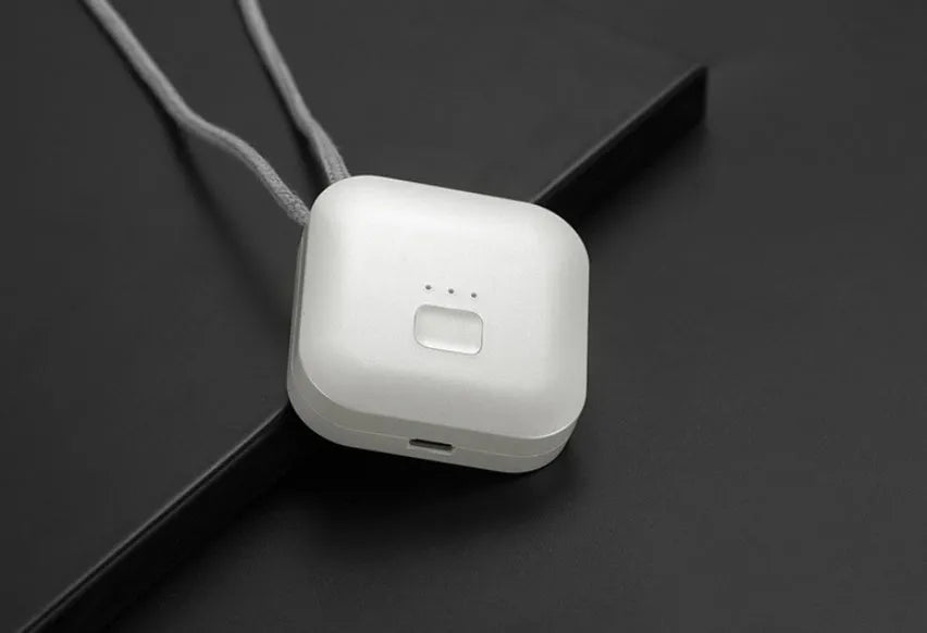 Small pink USB portable air purifier necklace on a table with charging cable.