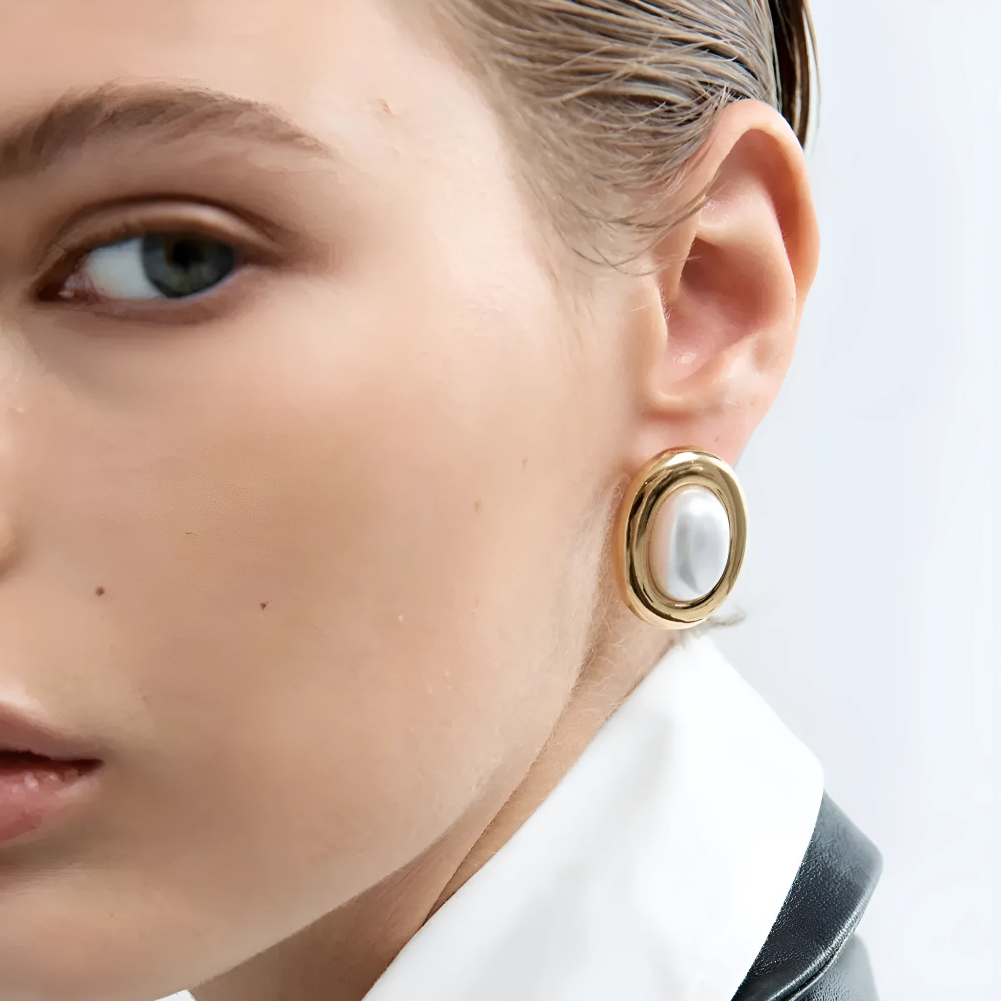 Small gold-tone stainless steel stud earrings with a white pearl accent on a grey background.