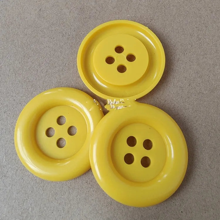 Plastic nylon oversized round button with four holes in various colours and sizes on a white background.