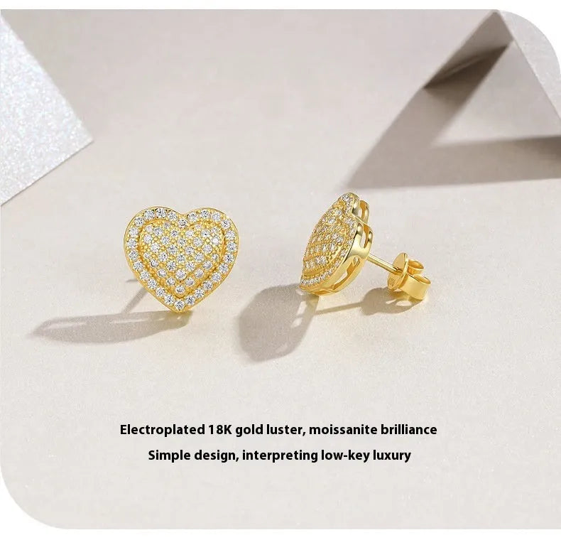 A pair of golden-colour heart stud earrings with a central moissanite stone, on a silver background.