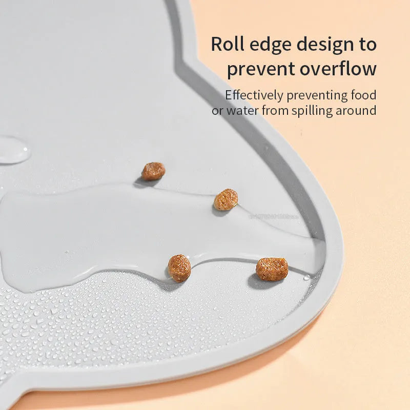 Solid colour silicone pet feeding mat in a cat head shape on a floor next to pet bowls.
