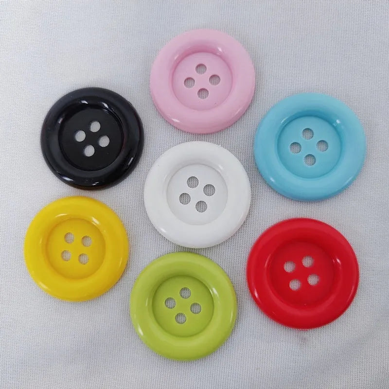 Plastic nylon oversized round button with four holes in various colours and sizes on a white background.