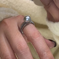 Copper geometric open ring with black pearl on a model's finger, showing adjustable gap.